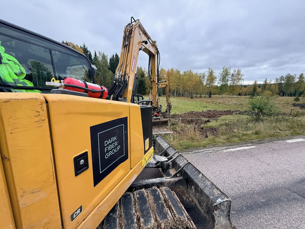 Dark Fiber Group-branded excavator at a roadside trench