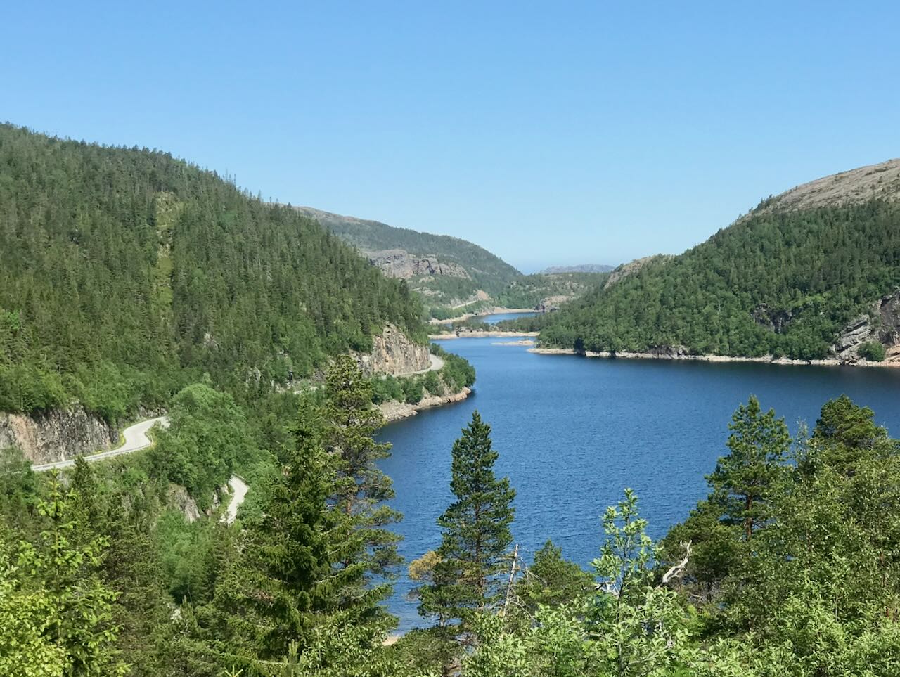 Forested hills and a winding road beside a deep blue Nordic lake